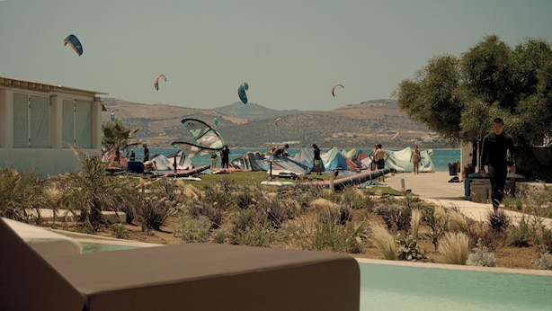 A pool area with lounge chairs, a view of the sea, and several kites in the sky. - Anapnoe Resort by ParosKite (Paros)