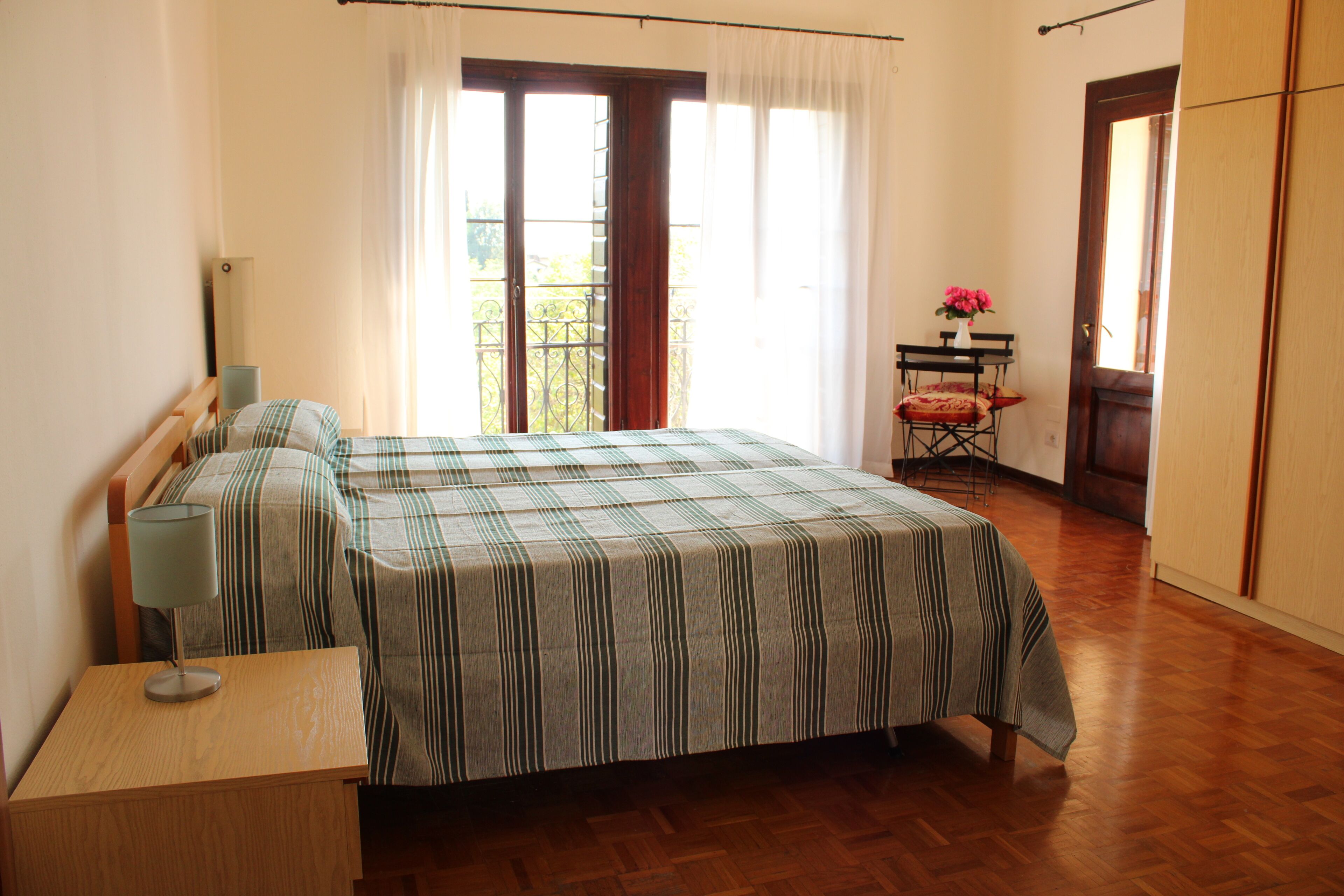 Un dormitorio con cama, mesita de noche, una silla y ventana con cortinas.