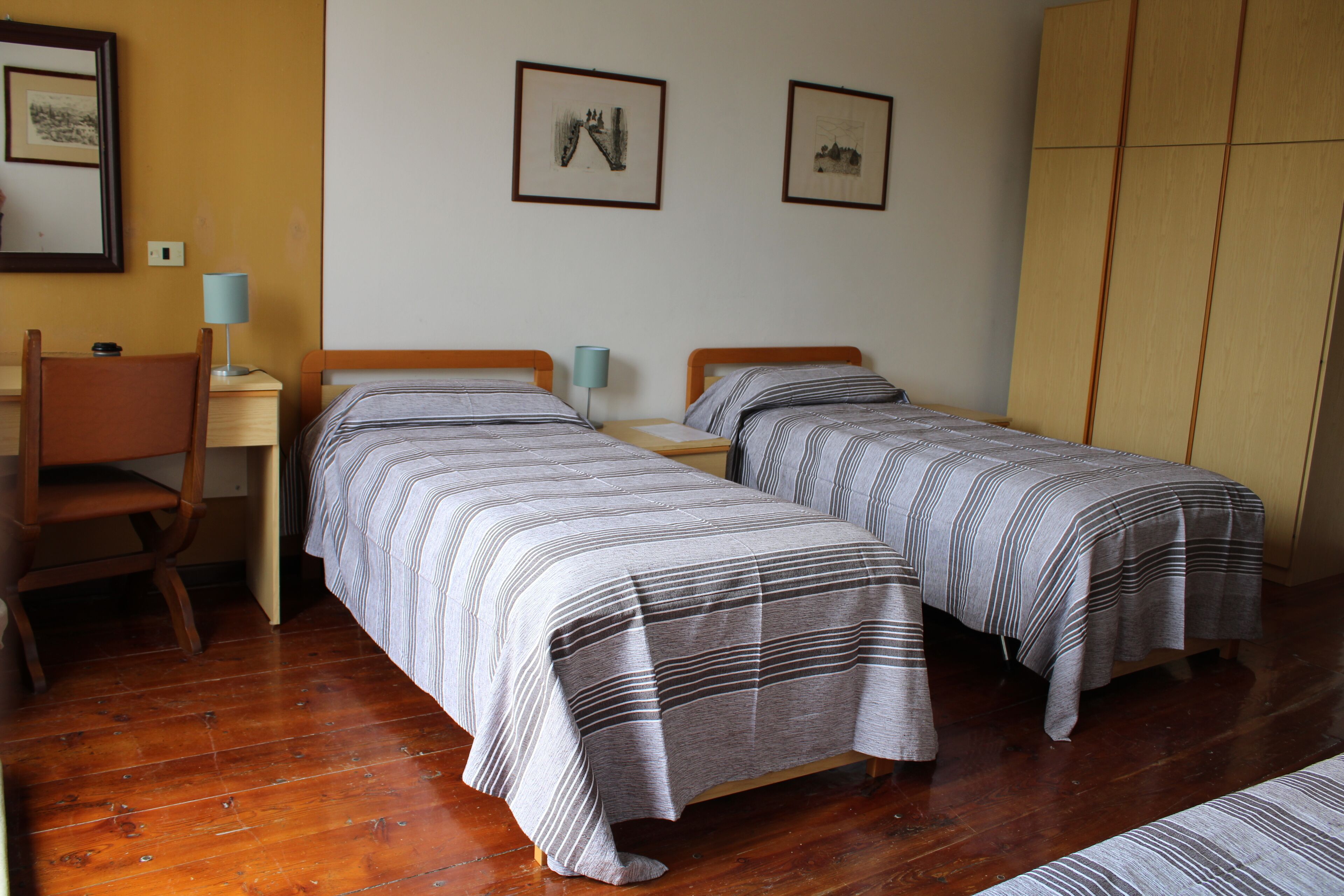 Ein Zimmer mit zwei Einzelbetten, einem Holztisch, einem Stuhl und einem Kleiderschrank.