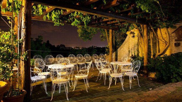 An outdoor patio with white metal chairs and tables, surrounded by greenery and a brick wall. - Villa Flangini (Asolo)