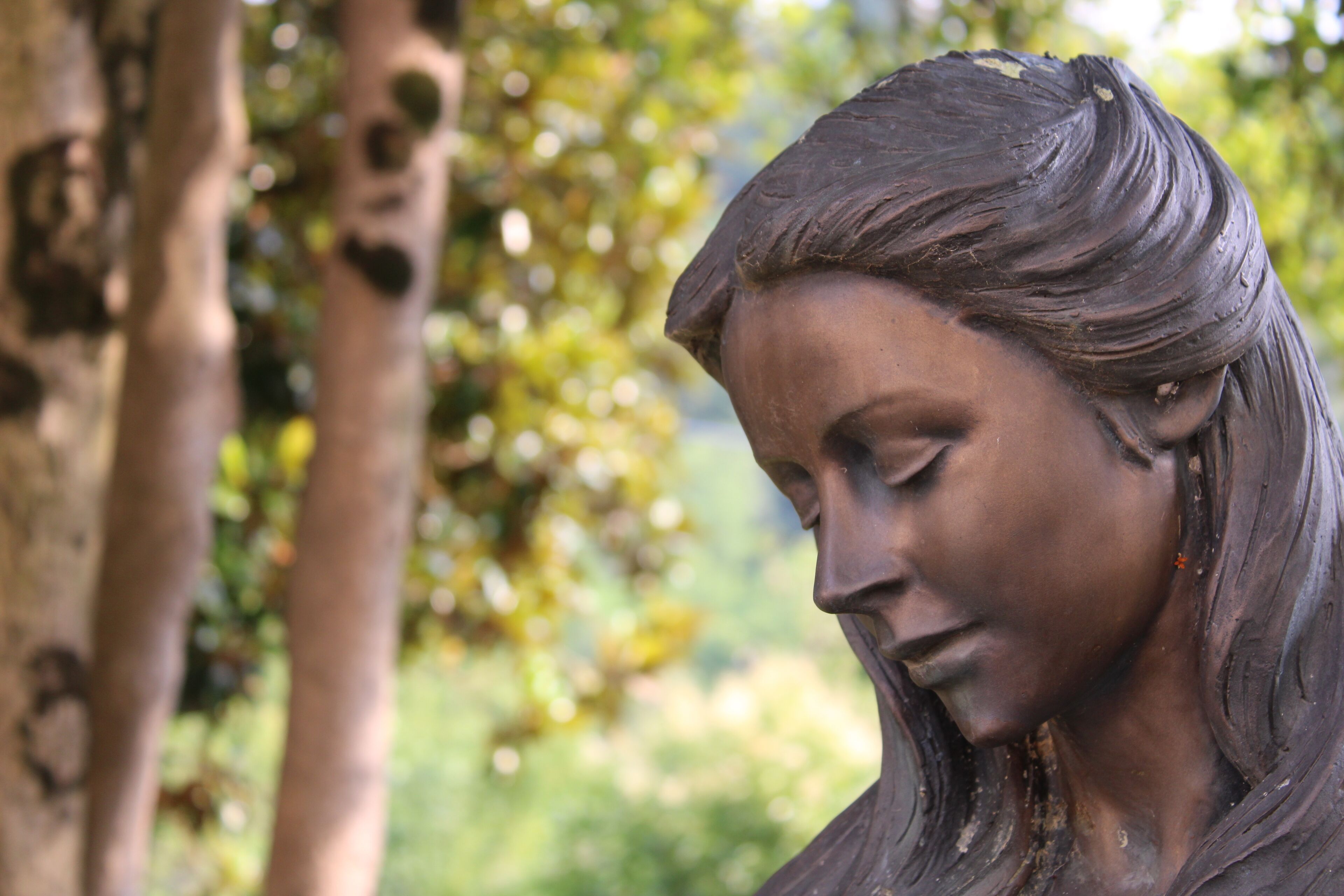 Eine Statue einer Frau mit langem Haar vor einer Baum- und Grünlandschaft.