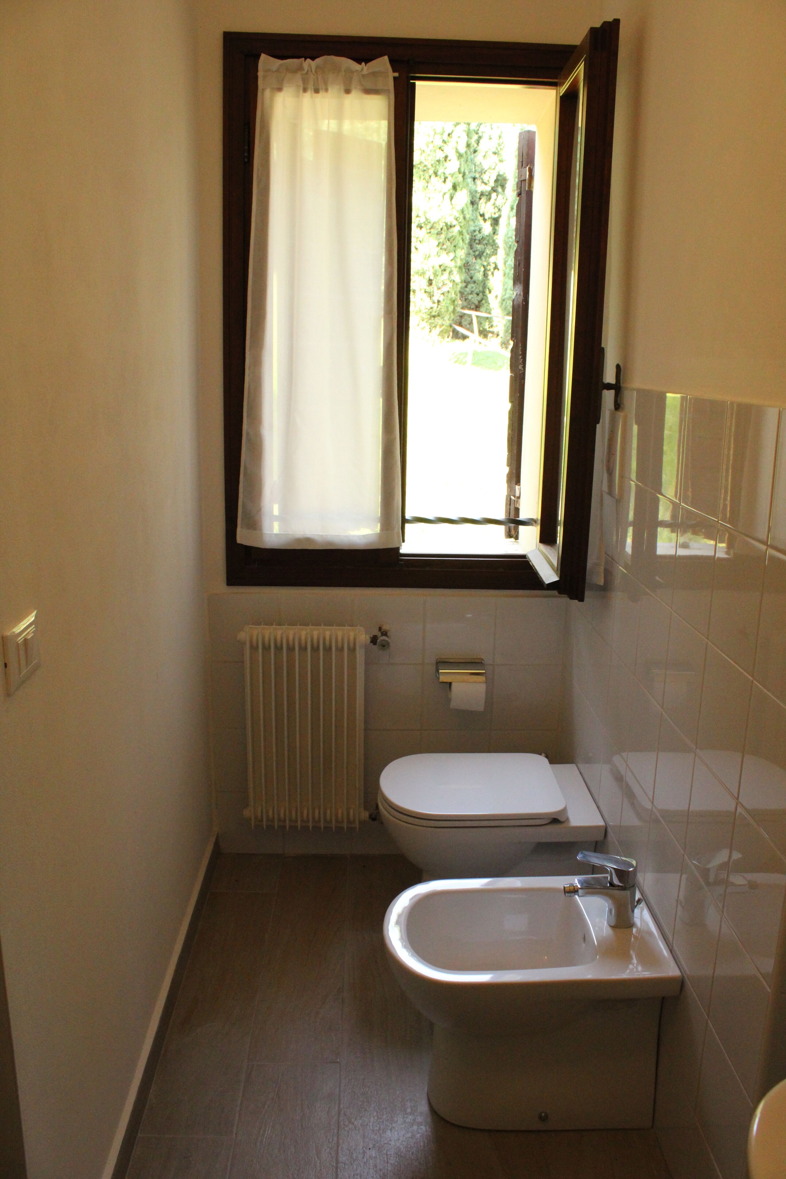 A small bathroom with a toilet, bidet, and a window with a curtain.