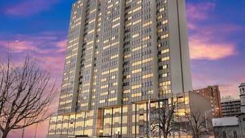 A tall, modern building with a grid of windows, surrounded by bare trees and other buildings.