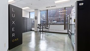Een moderne keuken met een zwart bord waarop 'LUXER ONE' staat, een zithoek met stoelen en grote ramen met uitzicht op gebouwen.