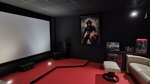Une salle de cinéma privée avec un grand écran, une moquette rouge, un canapé blanc et une affiche accrochée au mur.