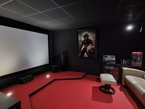 Une salle de cinéma privée avec un grand écran, une moquette rouge, un fauteuil inclinable et une affiche accrochée au mur.