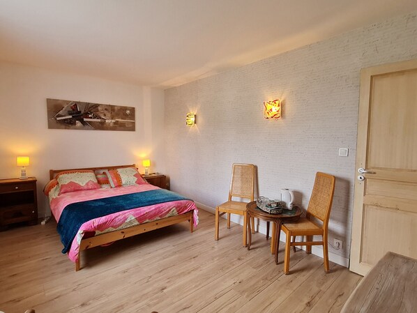 A bedroom with a bed, bedside tables, a chair, a small table with a kettle, and a door.