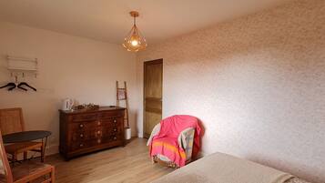 A bedroom with a wooden dresser, a chair, a bed with a patterned blanket, a hanging light fixture, and a door.