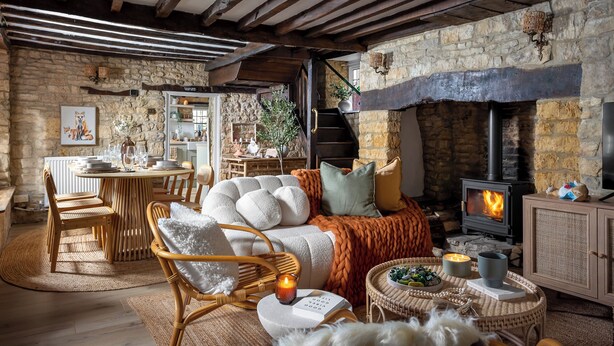 Un interior rústico con chimenea de piedra, vigas de madera, un comedor y una zona de estar acogedora.