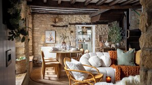 Un comedor rústico con pared de piedra, vigas de madera, sillas de mimbre y una mesa redonda dispuesta para comer.