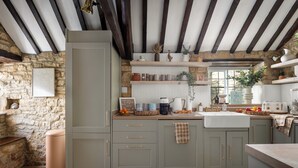 Una cocina rústica con paredes de piedra, vigas de madera y un lavamanos empotrado.