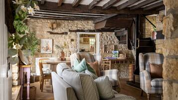 A rustic interior with stone walls, wooden beams, a fireplace, and a dining area.