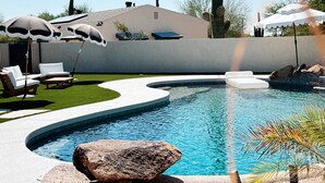 Une piscine à bord incurvé, dotée de chaises longues et de parasols.