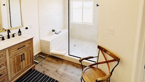 Une salle de bain moderne avec un meuble-lavabo en bois, une chaise indépendante, une douche dotée d’une porte en verre et un luminaire fixé au plafond.