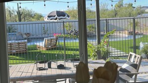 Une vue depuis une fenêtre donnant sur un patio, avec une piscine, du mobilier d’extérieur et un jardin clos.