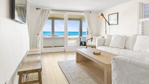 Een moderne, minimalistisch ingerichte kamer met een houten vloer, witte meubels en een groot raam met uitzicht op het strand.