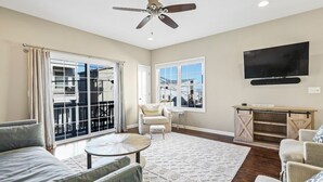 Ein Wohnzimmer mit einer Couch, Sesseln, einem Couchtisch, einem Fernseher und einem Deckenventilator.