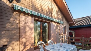A wooden cabin with a deck, a table with chairs, and a covered patio area. - Charming Pine Chalet - 4 Guests - Near Sanguinet Lake - Cleaning Included (Sanguinet)