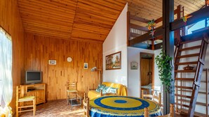 A cozy room with wooden walls and a tiled floor, featuring a bed, a TV, a dining table with chairs, and a wooden ladder. - Charming Pine Chalet - 4 Guests - Near Sanguinet Lake - Cleaning Included (Sanguinet)