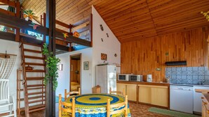 A cozy kitchen with wooden cabinets, a dining table with a patterned tablecloth, and a wooden ceiling. - Charming Pine Chalet - 4 Guests - Near Sanguinet Lake - Cleaning Included (Sanguinet)