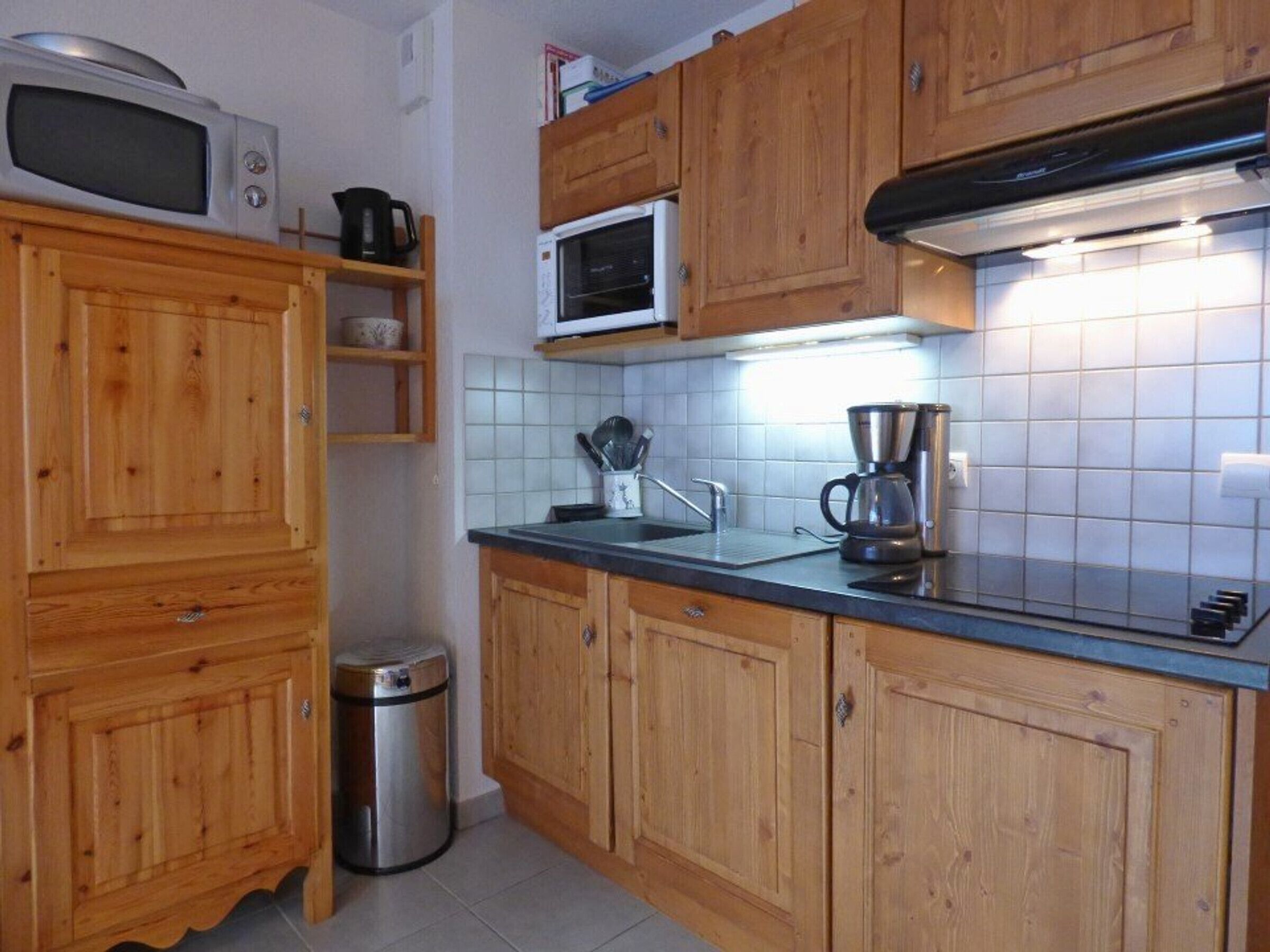 A kitchen with wooden cabinets, a microwave, a coffee maker, and a trash bin.