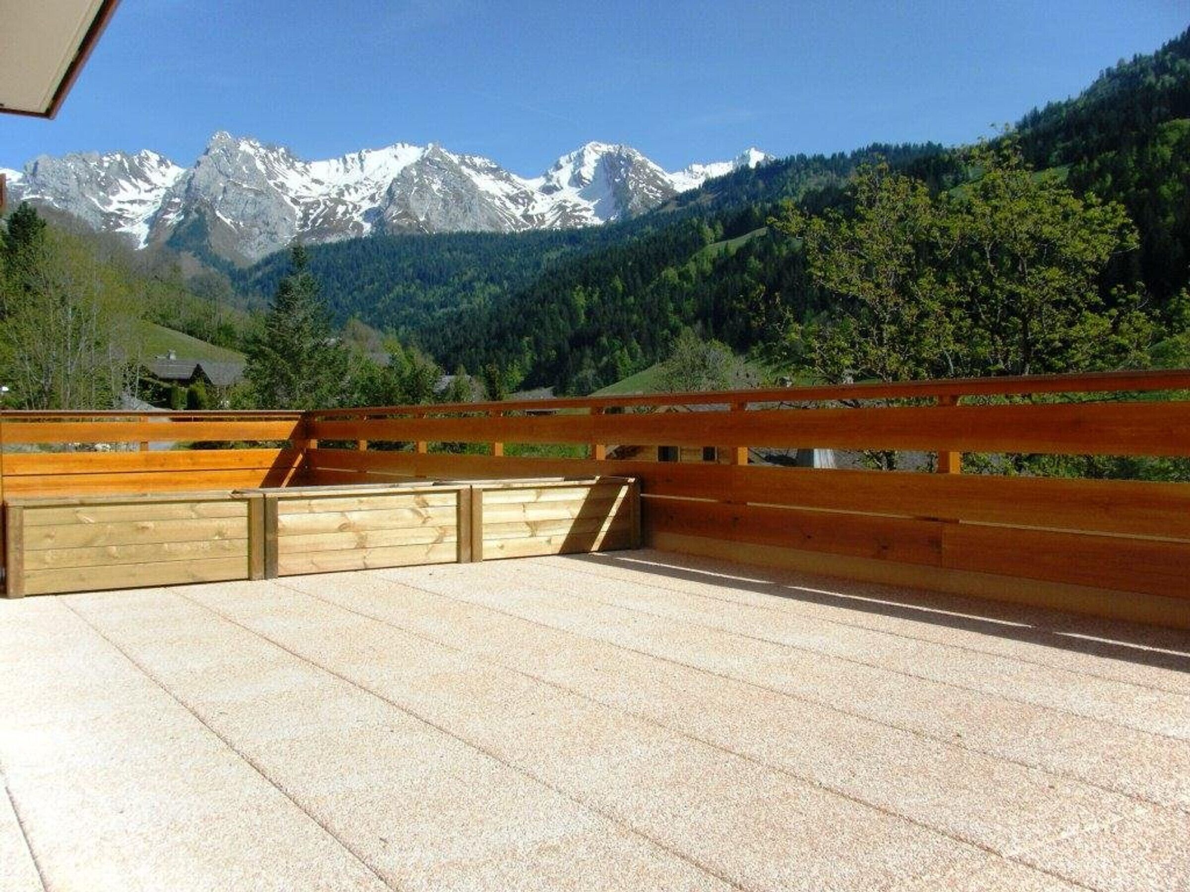 Une terrasse en bois offrant une vue sur des montagnes enneigées et des collines boisées.