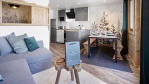 A modern living room with a grey sofa, a dining table with chairs, and a kitchen area with a microwave, oven, and sink. - Ski-in/Ski-out apartment with balcony and pets allowed (Val Thorens)
