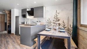 A modern kitchen with a central island, built-in appliances, and a dining area with a table and chairs. - Ski-in/Ski-out apartment with balcony and pets allowed (Val Thorens)