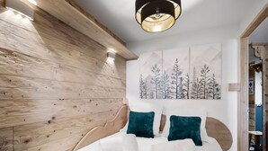 A modern bedroom with a wooden wall, a large bed with teal pillows, and a mountain landscape painting on the wall. - Ski-in/Ski-out apartment with balcony and pets allowed (Val Thorens)