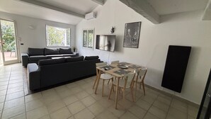 A modern living room with a sofa, dining table, chairs, and a TV. - Quiet villa in Balaruc with aircon and parking (Balaruc-les-Bains)