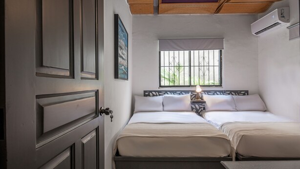 A bedroom with two beds, a window with bars, an air conditioner, and a door. - Escape Apartment in Gazcue Close to Colonial Zone (Santo Domingo)