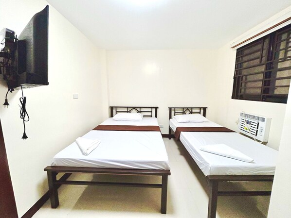 Una habitación con dos camas individuales, un televisor montado en la pared y una ventana con persianas.