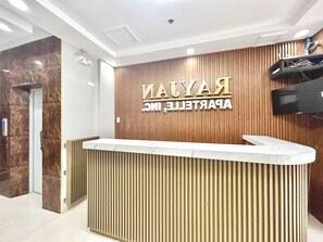 A reception desk with a wooden panel background and a marble counter. - OYO 1045 Rayjan Apartelle (Parañaque)
