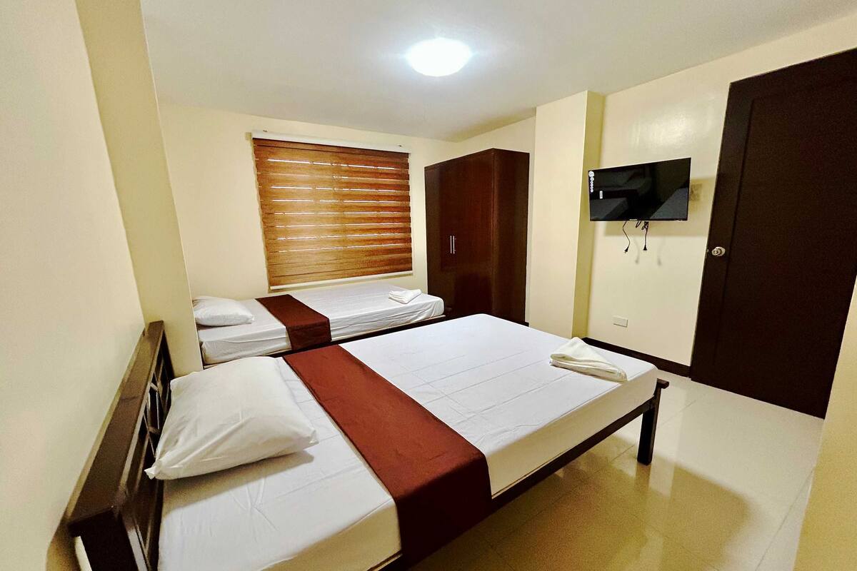A hotel room with two single beds, a wardrobe, a television, and a ceiling light.