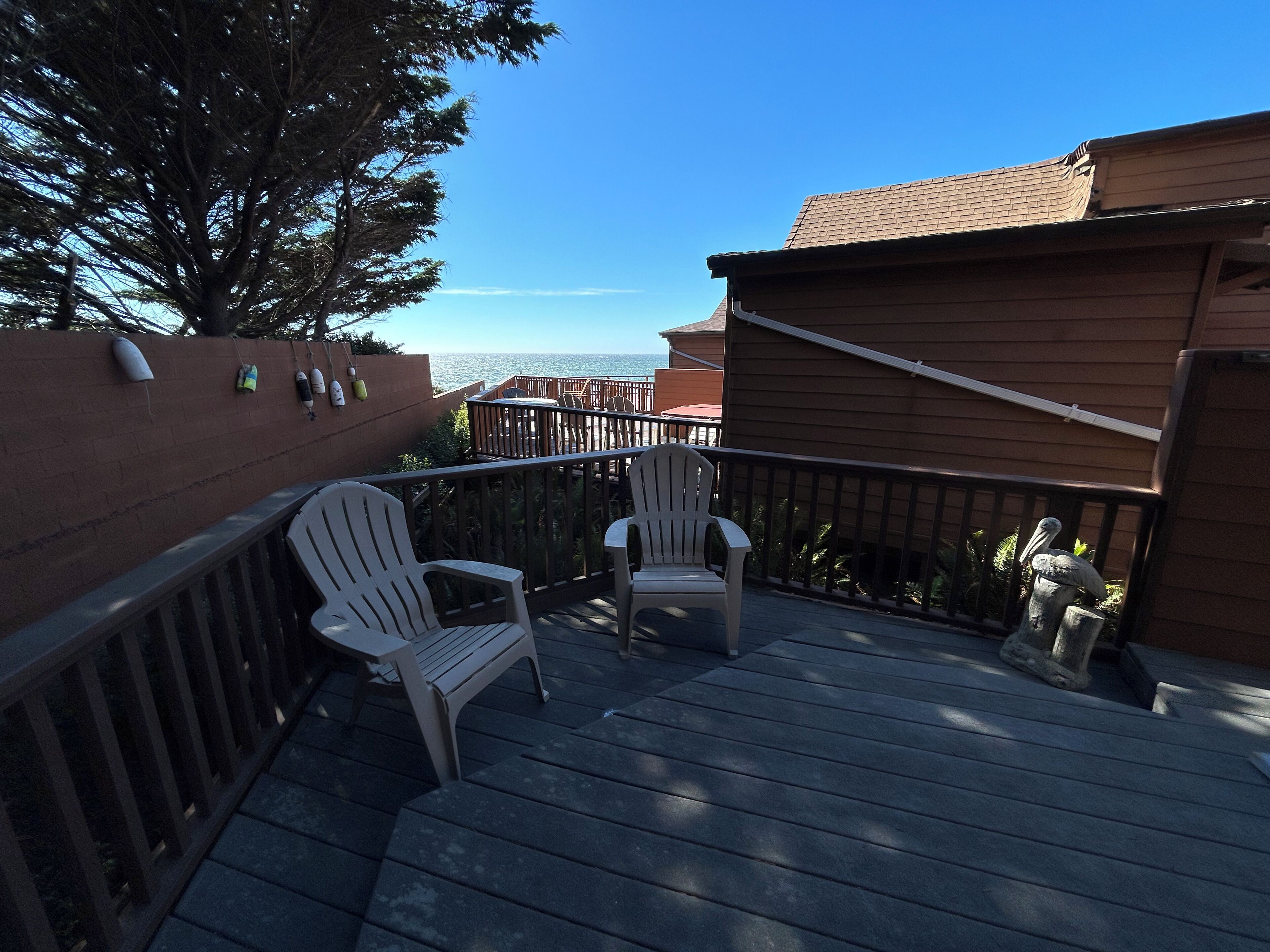 A wooden deck with two white Adirondack chairs, a railing, and a view of the ocean.