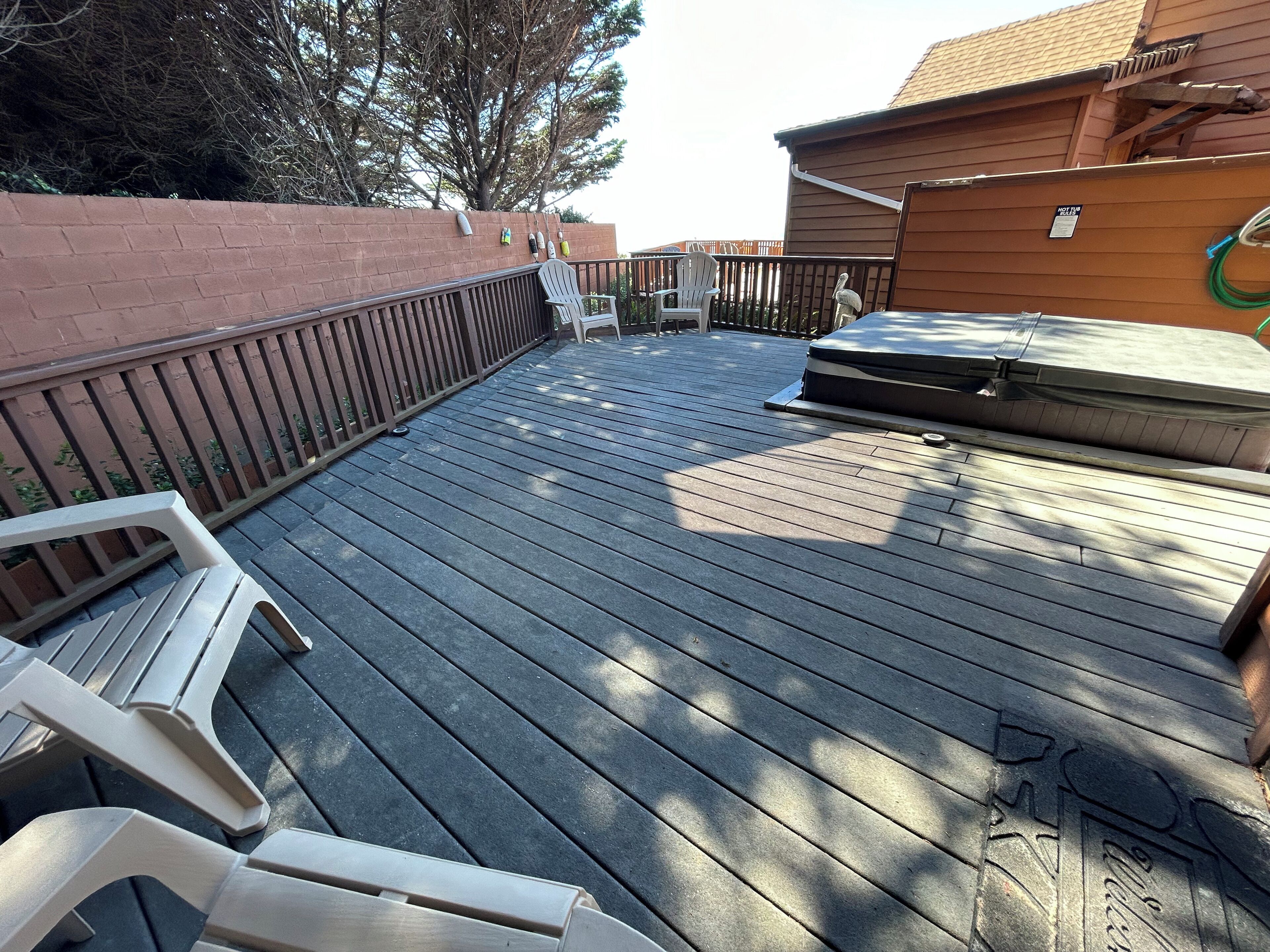 Une terrasse en bois avec un jacuzzi, un espace salon couvert et un mur en briques.