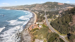Une route côtière, avec une plage d’un côté et une colline boisée de l’autre.