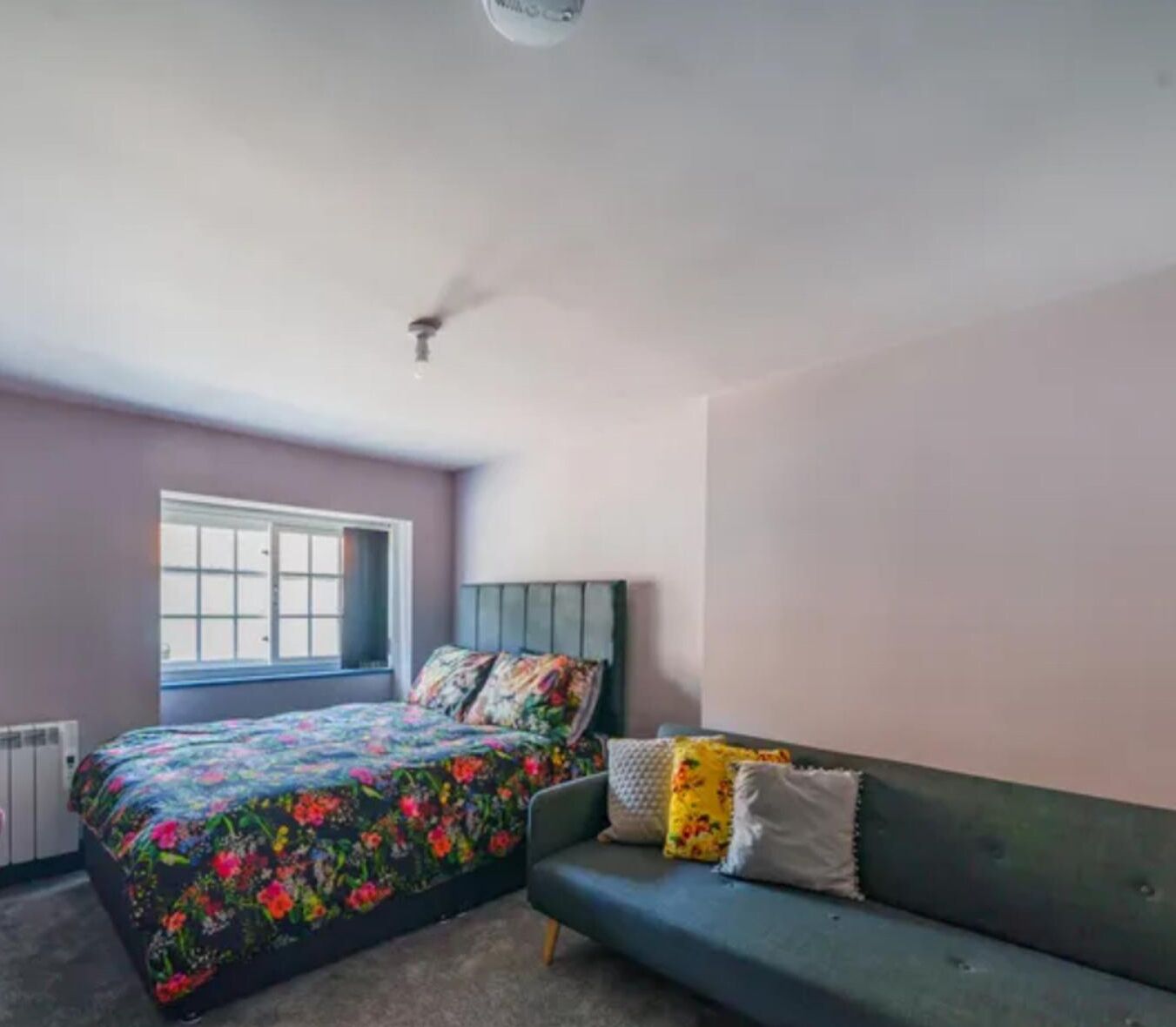 A bedroom with a bed, a window, a radiator, and a green sofa.