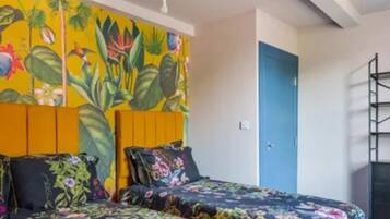 A room with a bed featuring floral bedding, a vibrant tropical mural on the wall, and a blue door.