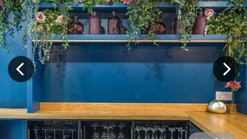 A bar area with shelves of glassware and decorative vases, a wooden counter, and a blue wall.