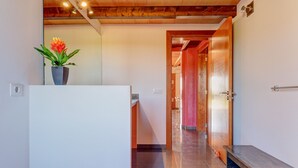 Un couloir avec un mur blanc, une plante en pot, un banc et une porte donnant sur une autre pièce.
