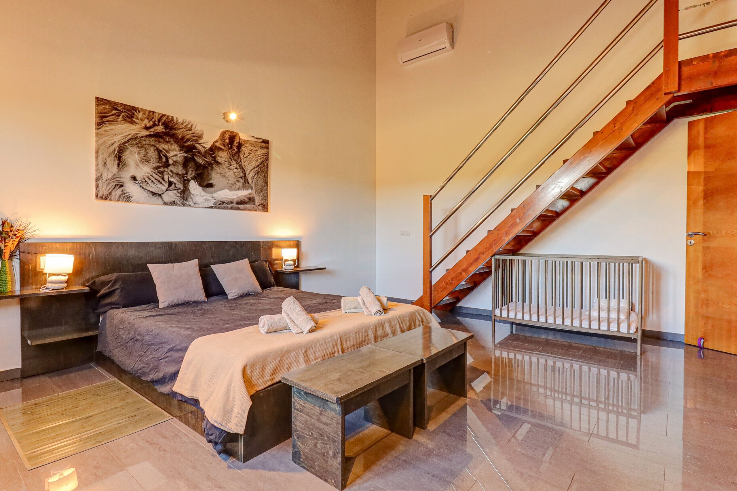 Een moderne slaapkamer met een groot bed, een houten bankje, een trap en een kunstwerk aan de muur.