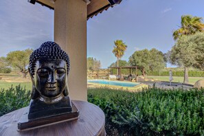 Una statua di Buddha su un piedistallo di legno, in un giardino con piscina e gazebo sullo sfondo.