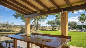 Une terrasse extérieure avec une table en bois et des bancs, entourée d’une pelouse et d’arbres.