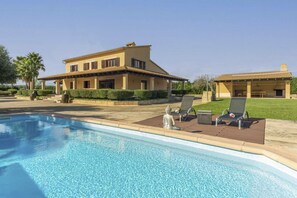 A poolside area with a large house, two lounge chairs, and a Buddha statue. - Son Mieres by Rentallorca (Petra)