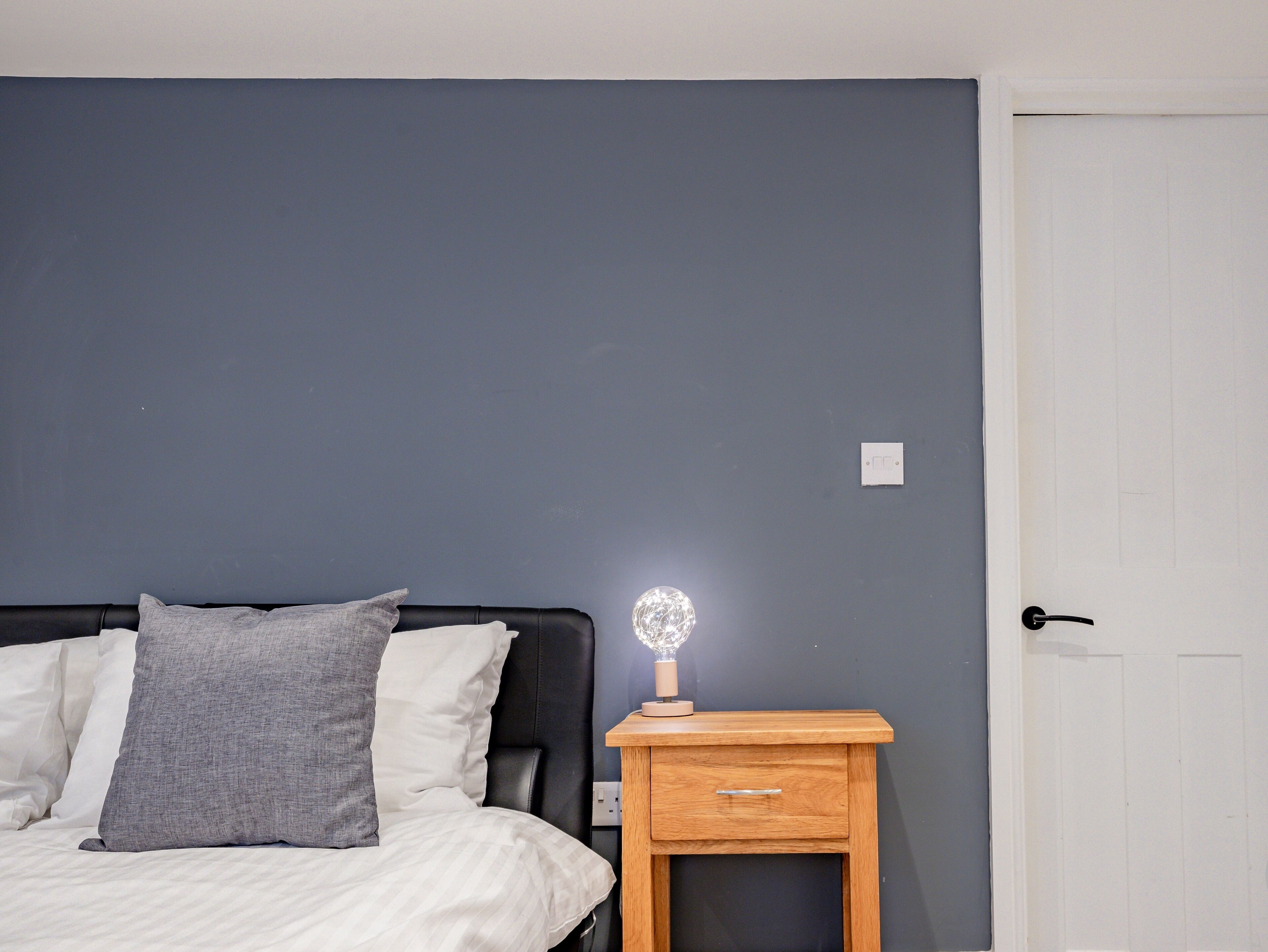 Quarto com uma cama, mesa de cabeceira e uma porta.