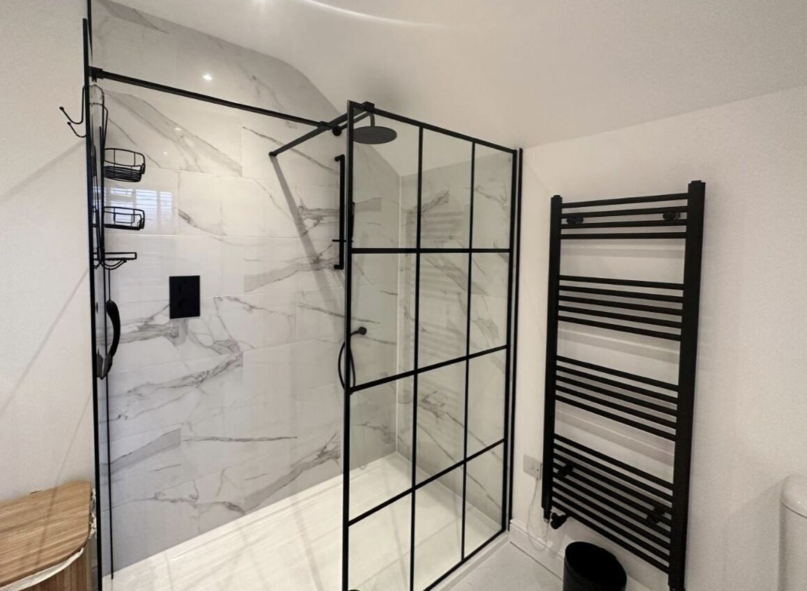 Une salle de bain moderne avec une douche à parois de verre, un porte-serviettes en métal noir et des murs en marbre.