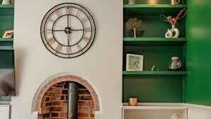 A cozy living room with a brick fireplace, a round wall clock, and green shelves with various decorations. - Exquisite renovation in central location (Hereford)