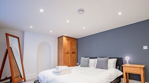A bedroom with a bed, a wooden wardrobe, a bedside table, and a mirror.