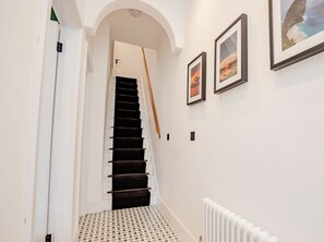 A hallway with a staircase, white walls, and framed pictures on the wall.